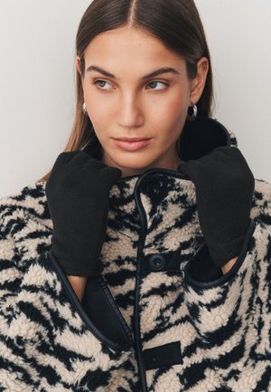 Kermanvärinen ja mustakirjailtu fleecetakki, jossa kaulus, nappikiinnitys ja mustat käsineet; sileä pintamateriaali ja mukavan väljä, runsas istuvuus.