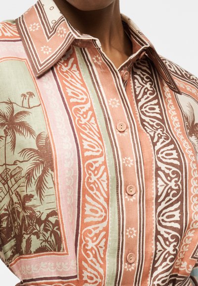 Κοντινή φωτογραφία πουκάμισου με κουμπιά, με κατακόρυφες ρίγες και πολύπλοκα σχέδια λουλουδιών και φοινικόδεντρων σε τόνους ροδακινί, καφέ, ροζ και πράσινου.