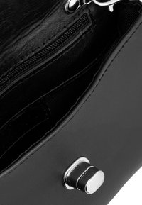 Interior de un bolso de cuero negro con un bolsillo con cremallera, textura suave y herrajes de plata. El diseño presenta líneas limpias y una costura duradera.