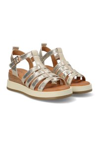 Sandali metallici oro con molteplici cinturini incrociati, un plantare imbottito marrone e una suola piattaforma beige con dettagli testurizzati.