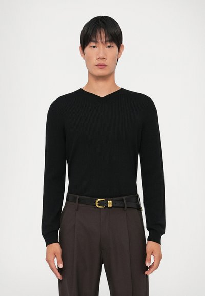 Sweater preto canelado de manga longa com um design em V. Usado com calças castanhas e um cinto preto com fivela em tom dourado.