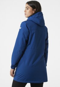 Blue insulated jacket with a hood, long sleeves, and a slightly tapered waist. Features zipper closures and side pockets. Smooth texture.