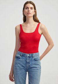 Bodysuit rojo acanalado con escote cuadrado y tirantes anchos, combinado con unos vaqueros de mezclilla azul claro de cintura alta.