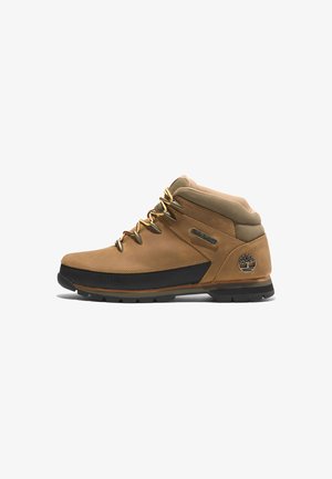 Braune Leder-Halbstiefel für Wanderungen mit schwarzen Gummisohlen, goldenen Ösen und gepolstertem Kragen. Timberland-Logo-Akzent an der Seite.