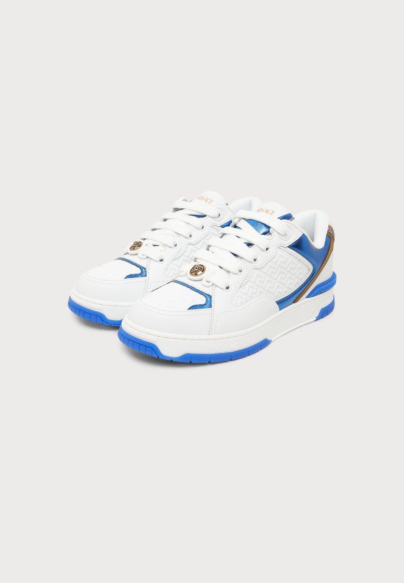 Paar weiße Low-Top-Sneaker mit blauen Akzenten, goldenen Details, gemusterten Seiten und dicken blauen Sohlen, auf einem schlichten hellen Hintergrund platziert.
