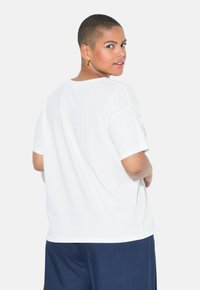 Witte oversized t-shirt met korte mouwen, ronde halslijn en zachte stof. Gecombineerd met donkerblauwe wijde broek.