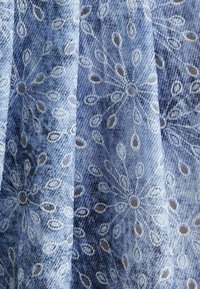 Blau gemustertes Stoff mit einer strukturierten Oberfläche, bestehend aus hellen und dunklen Blautönen und filigranen weißen Designs, die ein radiales Muster bilden.