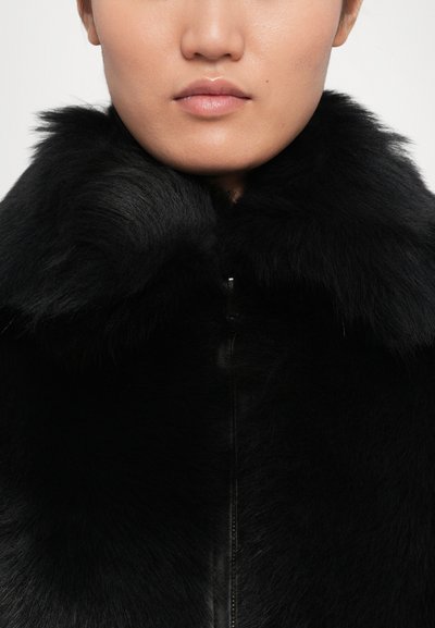 Close-up of a person wearing a black fur coat with a large collar and visible front zipper, showing lips and chin only.