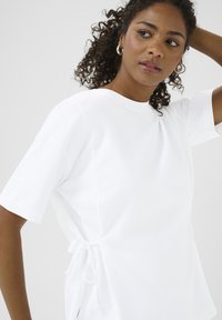Witte katoenen T-shirt met korte mouwen, voorzien van een zij-tie detail. Glad textuur en een relaxte pasvorm in een minimalistisch ontwerp.