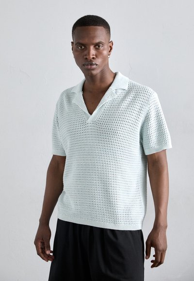 Polo shirt in maglia blu chiaro con un motivo in mesh testurizzato, maniche corte e colletto a coste. Indossato con pantaloni corti neri.