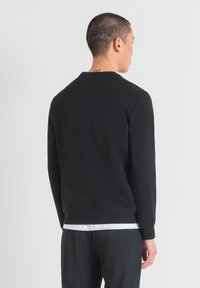 Sudadera negra con cuello redondo y mangas largas, hecha de una tela suave. Presenta puños y dobladillo de canalé. Diseño liso, sin logos visibles.