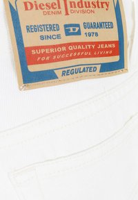Tessuto di denim bianco con un'etichetta visibile che presenta un testo rosso e blu. L'etichetta indica i dettagli del prodotto e l'assicurazione di qualità.