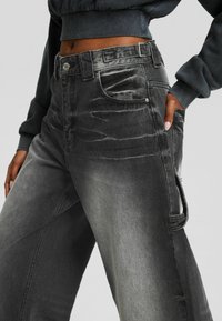 Beskuren vy av en person som bär blekta svarta vida jeans med en sidoficka och en avkortad mörkgrå sweatshirt.