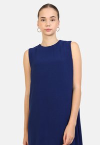 Vestito senza maniche di colore blu scuro con una texture liscia. Presenta un collo a giro e una vestibilità comoda che arriva appena sopra il ginocchio.