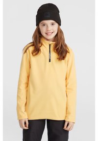 Gul fleece-pullover med kvart dragkedja, svart dragkedjedetalj och långa ärmar. Bärs med en svart stickad mössa. Slät textur.