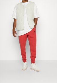 Ljusgrå quiltad väst över en vit t-shirt, tillsammans med röda sweatpants och vita sneakers. Har Nike-loggor på västen och byxorna.