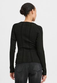 Svart rippad stickad tröja med långa ärmar och rund halsringning, med en kroppsnära passform som framhäver midjan och med en texturerad mönstring.
