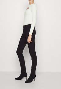 Vit ribbad långärmad topp med en utskärning, i kombination med figurnära svarta byxor och spetsiga svarta ankelstövlar.