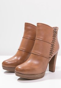 Bottines en cuir marron avec une finition lisse, deux bandes horizontales et un lacet sur le côté. Présentent un talon épais et une semelle plateforme.