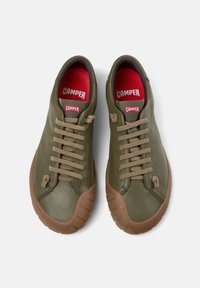 Αθλητικά παπούτσια από δέρμα ελιάς με καφέ λαστιχένιες σόλες, μπεζ κορδόνια και κόκκινη εσωτερική επένδυση. Διαθέτουν στρογγυλεμένη μύτη και διακριτικές ανάγλυφες λεπτομέρειες.