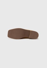 Suela de zapato de goma marrón con un patrón de agarre texturizado, que presenta un tacón ligeramente elevado y una puntera redondeada. Bordes suaves y acentos mínimos.