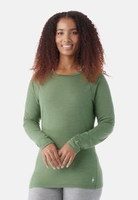 Grünes Langarmshirt mit rundem Ausschnitt, weicher Textur und Akzentnähten. Beinhaltet ein kleines Logodetail nahe dem Saum.