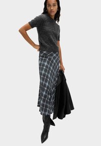 Grauer kurzärmliger Pullover kombiniert mit einem langen karierten Rock in Blau und Weiß, ergänzt durch schwarze kniehohe Stiefel und eine schwarze Jacke.