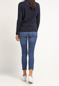 Marinblå stickad tröja med ribbad nederkant, kombinerad med slim-fit blå jeans och vita sneakers. Designen har långa ärmar och rund halsringning.