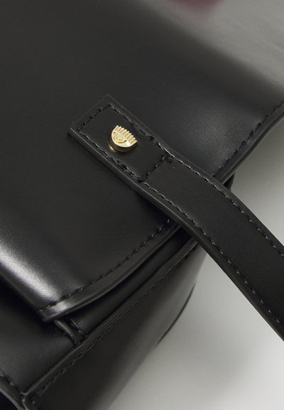 Black leather handbag featuring a smooth texture, a folded flap closure, and a gold-tone metal accent on the strap.