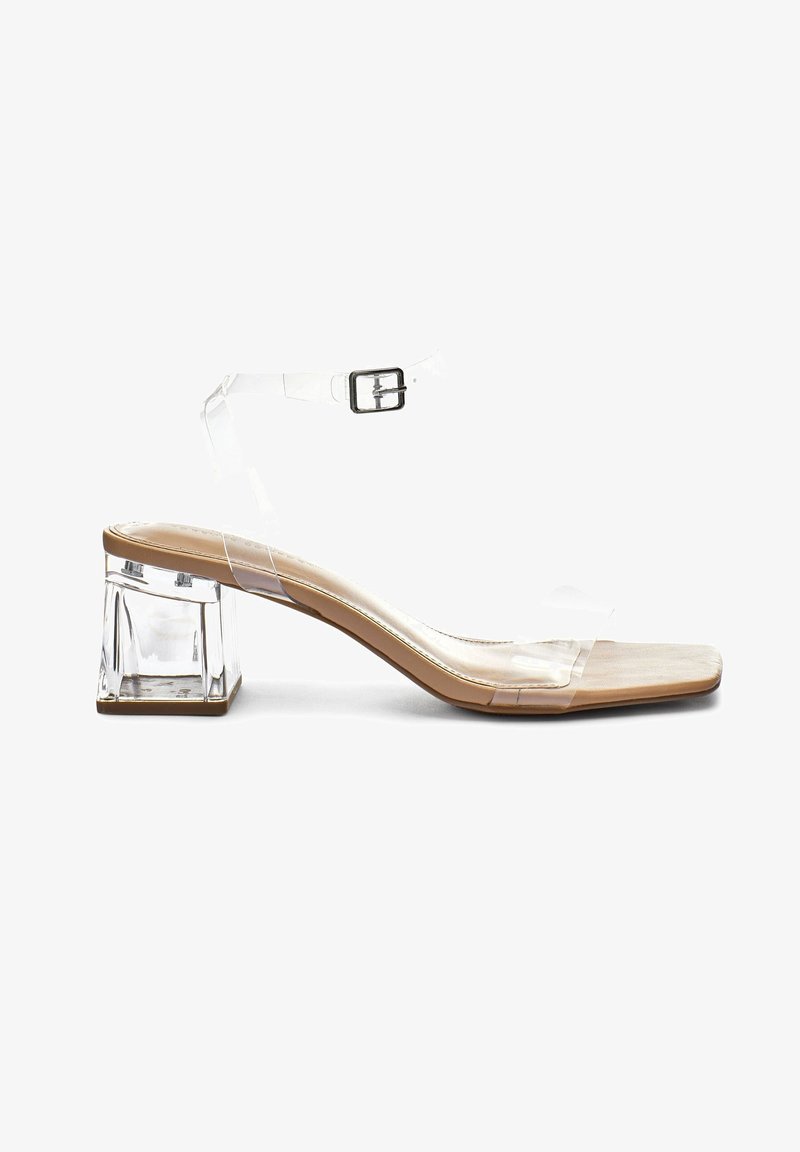 Sandale à talon clair avec une bride transparente, un bout carré et un talon bloc. La semelle présente une teinte naturelle, mettant en valeur le design élégant.