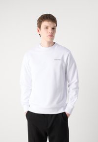 Sudadera blanca con cuello redondo, mangas largas y puños acanalados. Presenta un pequeño logo negro de Calvin Klein en el lado izquierdo del pecho.