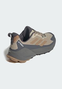 Beige og grå Adidas Terrex trailløbesko med brune detaljer og tekstureret sål, vist fra en bagside vinkel på hvid baggrund.
