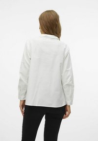 Chemise blanche à manches longues avec col et poignets à boutons. Vue de dos avec une silhouette droite et une légère fente à l'ourlet, fabriquée dans un tissu lisse.