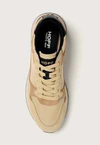 Sneaker sportivo beige realizzato in materiali scamosciati e tessili, con dettagli testurizzati, punta tonda e lacci robusti. Presenta un'etichetta nera sulla soletta.
