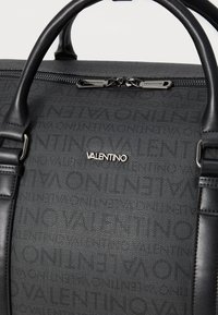 Saco de tecido preto com um design texturizado e o logótipo "Valentino". Inclui alças duplas e um fecho com zíper com hardware em tom prateado.