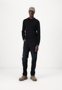 Maglione nero a maglia con scollo a V, abbinato a jeans blu scuro e scarpe beige con lacci. Un cappellino grigio chiaro con la ricamatura "Won".