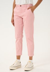 Pink cotton trousers with a straight cut, featuring a button closure and side pockets, styled with white sneakers.