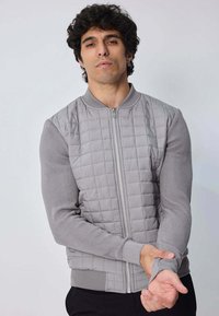 Veste bomber grise avec un devant matelassé et des manches côtelées. Comprend une fermeture éclair et un col rond, mettant en valeur un design texturé.