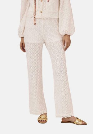 Pantalones de encaje rosa claro con un patrón de diamantes, forma acampanada y dobladillo con forma de concha. Combinados con sandalias doradas y una blusa blanca texturizada.