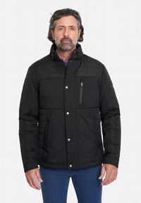 Chaqueta acolchada negra con un alto cuello, cierre frontal con cremallera y cierres a presión. Presenta costuras horizontales y dos bolsillos laterales.