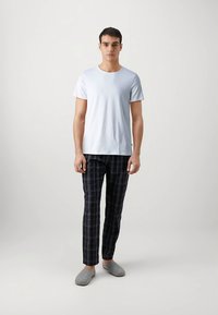 Balta kokvilnas T-krekls, tumši zili rūtainas pidžamas bikses un pelēkas čības. Vienkāršs dizains un ērtas piegriezums.