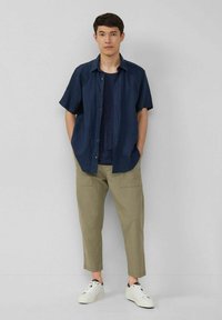 Short-sleeve navy button-up shirt, layered over a dark t-shirt, with beige cropped pants and white sneakers, plain design, no visible patterns.