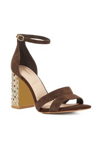 Brown suede heeled sandal with crossed straps and a buckled ankle strap. Features a geometric faceted block heel with a gold accent and clear stones.