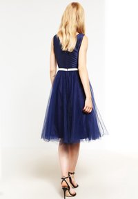 Námořnické modré šaty s těsným korzetem a rozšířenou tylovou sukní. Obsahují bílý pas a zipové zapínání na zadní straně.