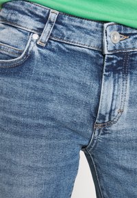 Vaqueros de denim azul con corte recto, diseño de cinco bolsillos y costuras en naranja contrastante en las costuras. Cierre de botón en la cintura.