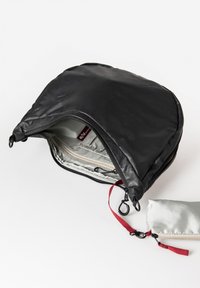 Zwarte nylon tas met een ronde bovenkant, voorzien van een ritssluiting, een lichtgrijze binnenkant en een afneembare zilveren pouch met rode accenten.