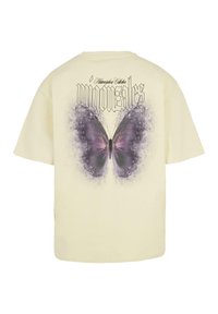 Camiseta de color crema que presenta un gran gráfico de mariposa púrpura en la parte posterior, con el texto "m Gonzales" en una fuente ornamentada encima.