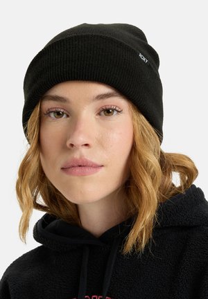 Schwarze Strickmütze mit einem gerippten Muster und einem kleinen weißen "ROXY"-Logo. Getragen von einer Person mit welligem Haar, kombiniert mit einem schwarzen Hoodie.