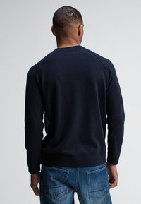 Donkerblauwe, gebreide trui met een ronde hals en raglanmouwen, gecombineerd met lichtblauwe jeans met twee achterzakken.