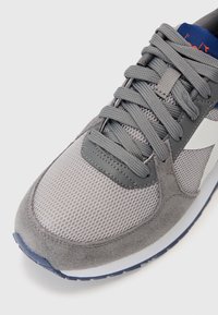 Gray athletic shoe with mesh and suede materials, featuring gray laces, a rubber sole, and a white accent logo on the side.